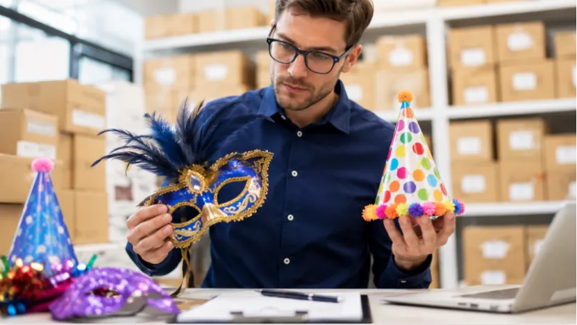 A buyer inspecting a feathered masquerade mask and a party hat in a warehouse