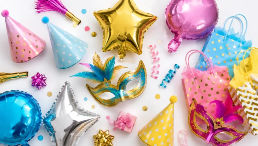 Colorful flat lay of assorted party supplies including hats, foil balloons, and masks