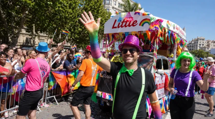 Participants in colorful costume accessories marching next to a decorated float in a lively parade